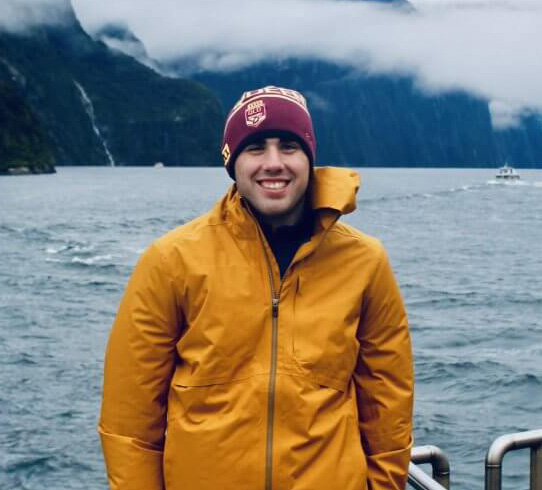 Jack Tamisiea on a boat wearing slicker and cap, mountains in background