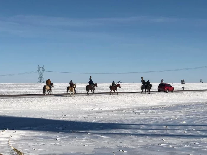 Riders on horseback proceed across a snowy field