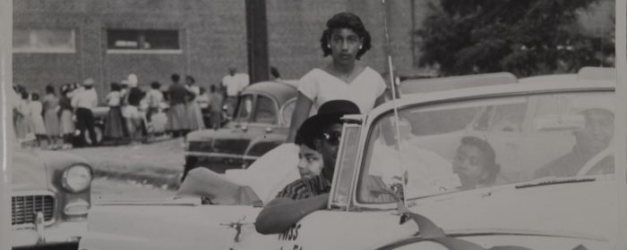 Young African American woman stares at camera from back of open convertible