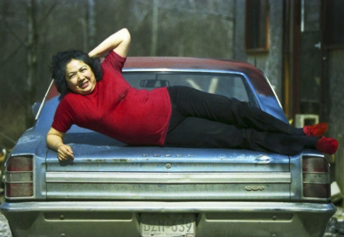 Woman in red shirt poses on trunk of car