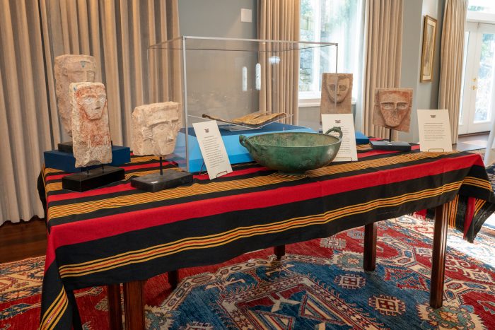 Collection of artifacts including bowl and stelae on table with striped cloth