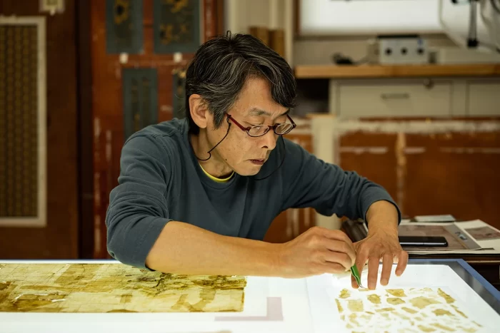 Jiro Ueda works with tweezers to repair damaged document on lightboard