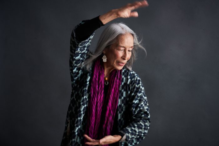 Older Asian woman with long gray hair dancing with one arm raise dover her head