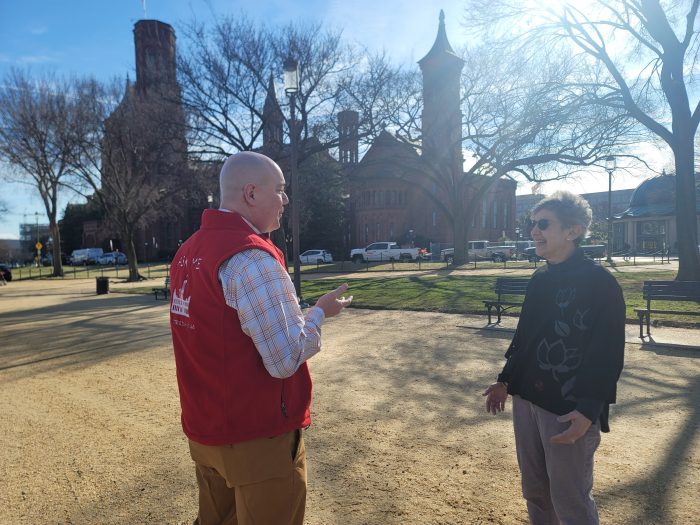 Volunteer in red vest speaks to passerby on the National Mall