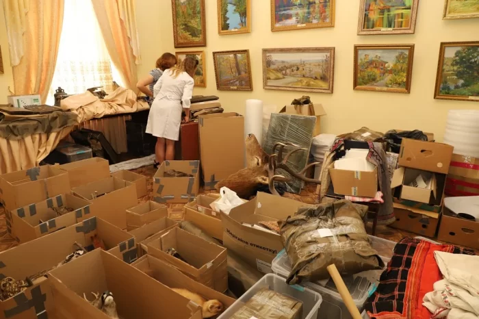 Woman in white smock stands amidst boxes of artifacts