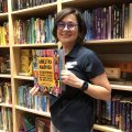 Cindy Pol poses in front of library shelves while holding a book