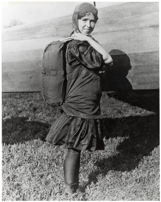 Woman in skirt with cap and parachute standing next to plane