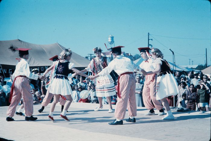 Visitors dancing with performers in traditional clothing and hats