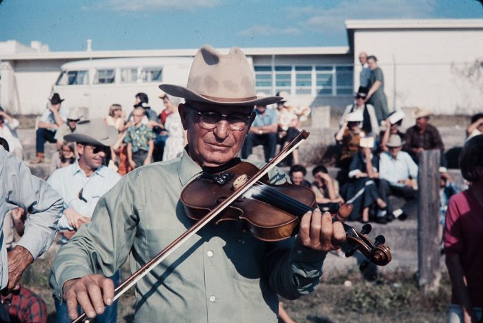 An older man wearing a cowboy hat plays the fiddle