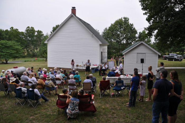 People sitting in folding chairs outside small clapboard building