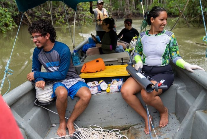 Barefoot researchers (named in caption) on boat in mangrove swamp