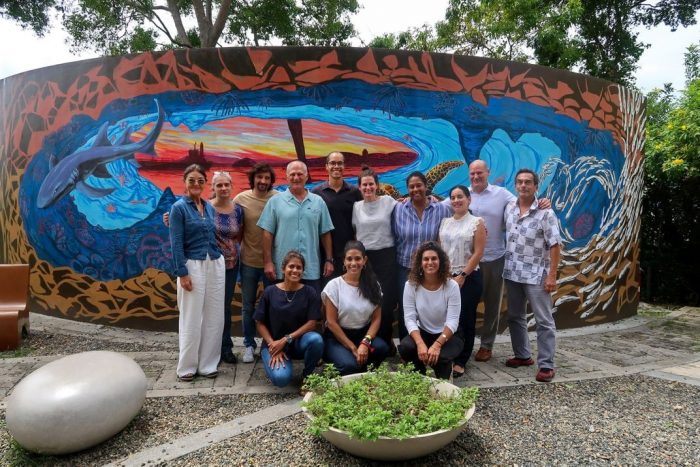 Researchers named in caption pose for group shot in front of mural depicting ocean and sunset