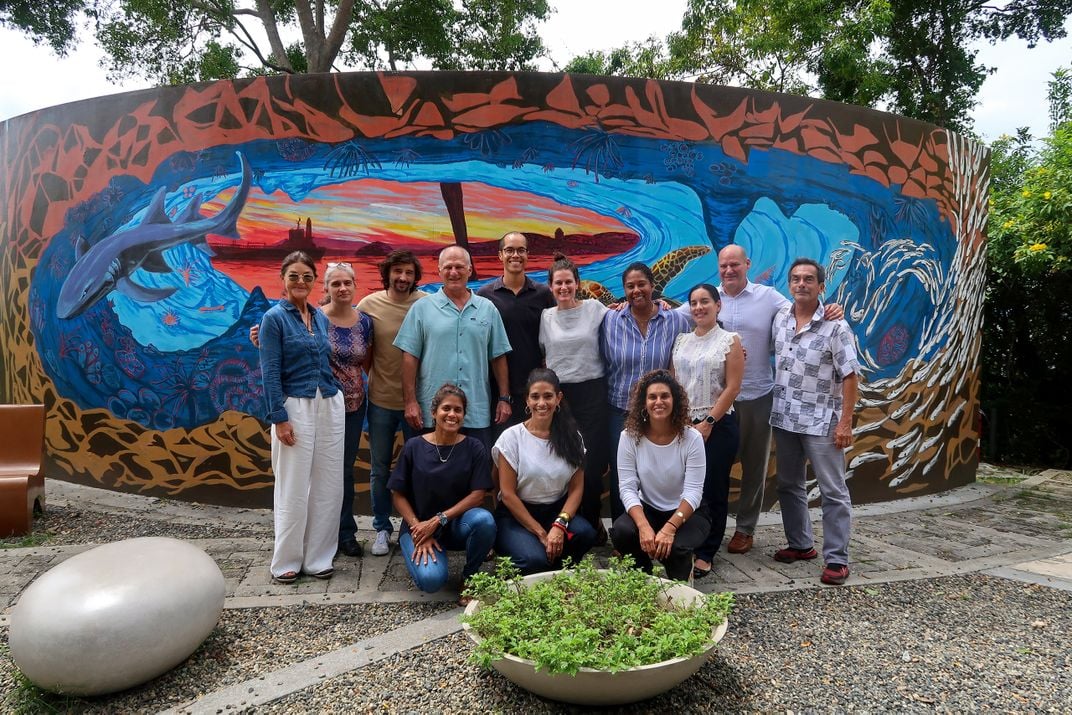 Researchers named in caption pose for group shot in front of mural depicting ocean and sunset