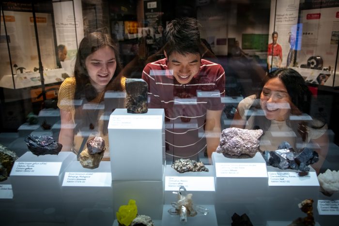 Three young people smile and laugh while looking at minerals in display cases