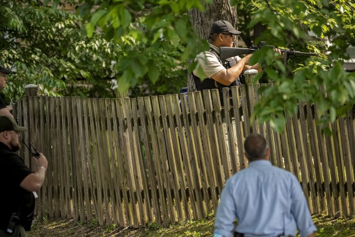 NZP Officer Sookchayee  stands next to fence aiming rifle