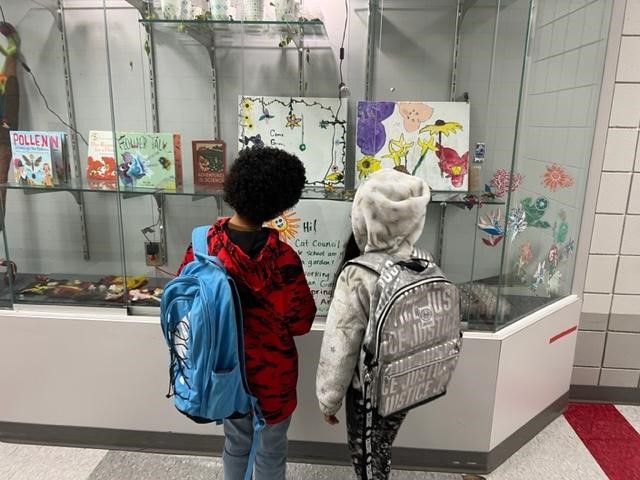 Two small children look at display case of student garden drawings