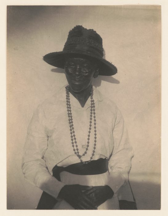 Black and white photo of  of black woman wearing a hat and beaded necklace by Doris Ulmann