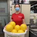 Volunteer in red shirt wearing mask holds a basket full of yellow balls