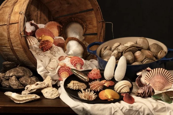 Still life photo of bushel basket spilling various bivalves and mollusks on to a table