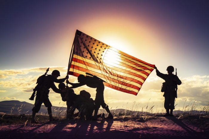 Soldiers raising American flag, seen in silhouette