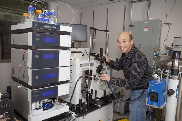 Newsome in black and white shirt grins in front of equipment