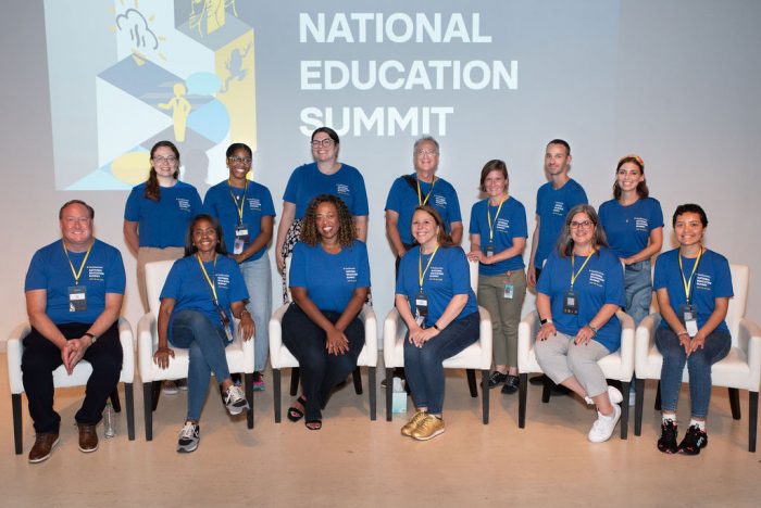 Staff in blue t-shirts pose for group photo at Education Summit