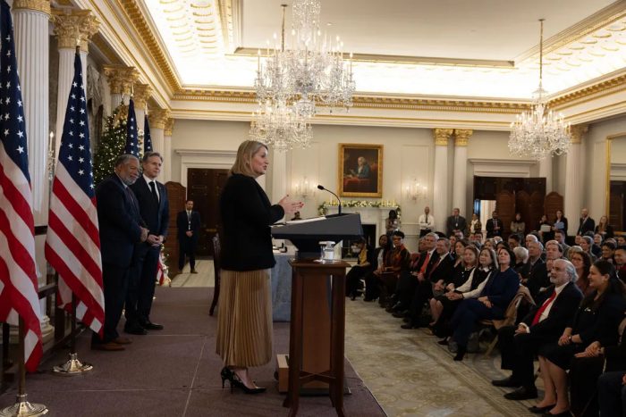 Liz Allen addresses gathering at State Department. Secretaries Blinken and Bunch stand behind her.