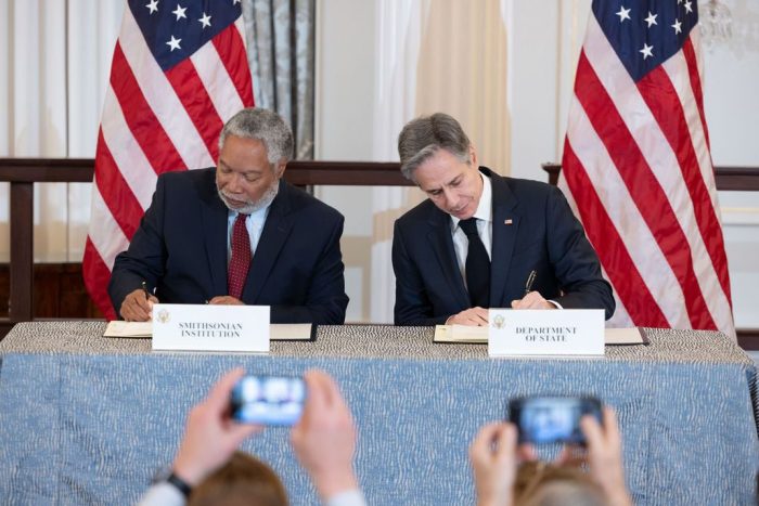 Secretaries Bunch and Blinken sign agreement while seated at table