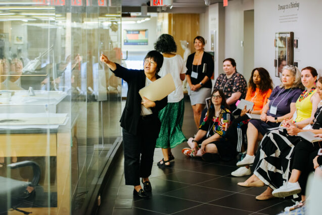 Students listen to docent explaining artworks in display case