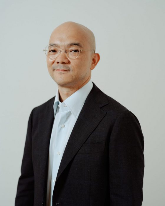 Formal portrait of Aaron Seeto in black jacket, white shirt against pale background