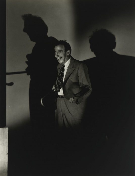 Shadowy portrait of Jimmy Durante with cane, mugging for camera