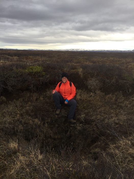 Martin in orange parka sits on a moor with tumultuous sky in the background