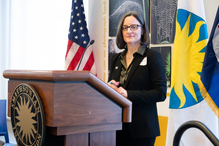 Canonico stands at podium with Smithsonian seal, flanked by SI and US flags