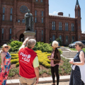 Volunteer in red vest talks to group of women while pointing to Smithsonian Castle