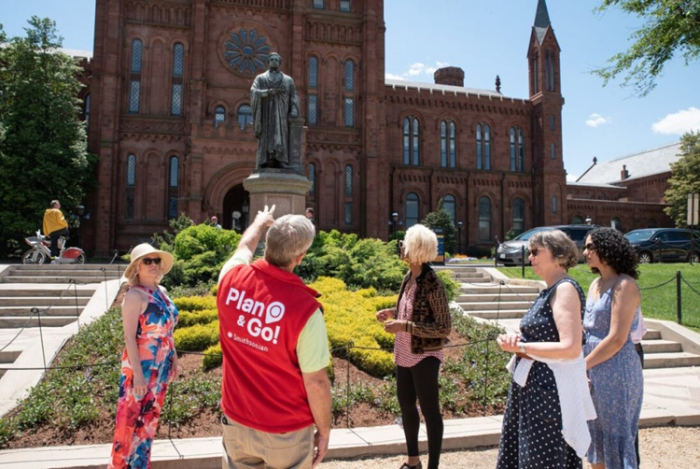 Volunteer in red vest talks to group of women while pointing to Smithsonian Castle