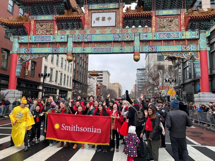 Group photo of parade participants holding red Smithsonian banner under ornate Chinese gate in Washington, DC