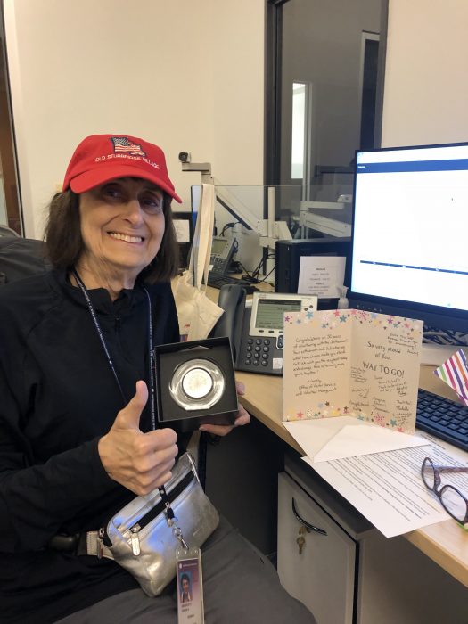 DeCorleto, wearing red ball cap displays her medal for 50 years of service