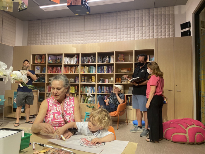 Older woman, children and adults look at books in library setting