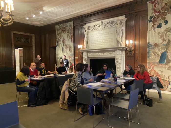 Teachers gathered at tables having a discussion in paneled room with ornate fireplace