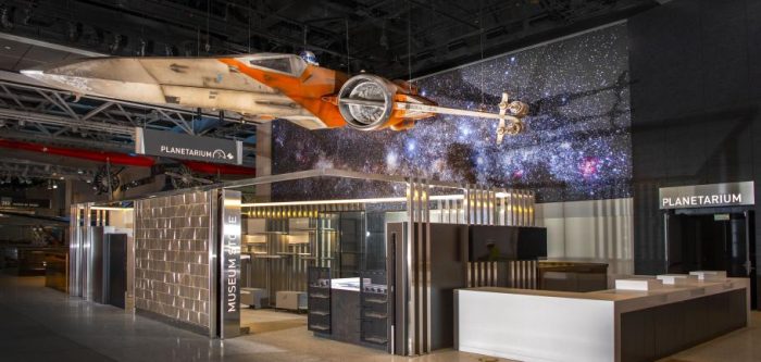 Starfighter movie prop hangs in front of planetarium backdrop showing starry outer space