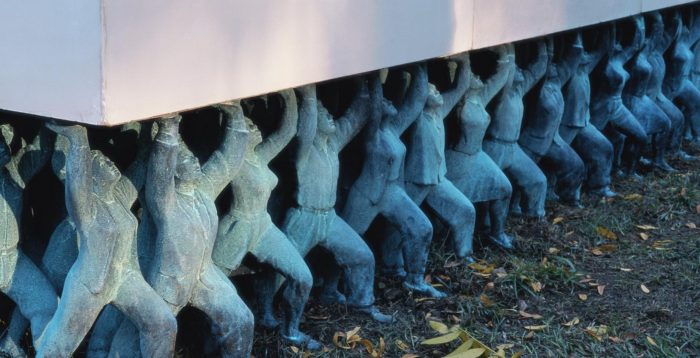 Detail of sculpture installation "Public Figures" showing statues of people holding up plinth