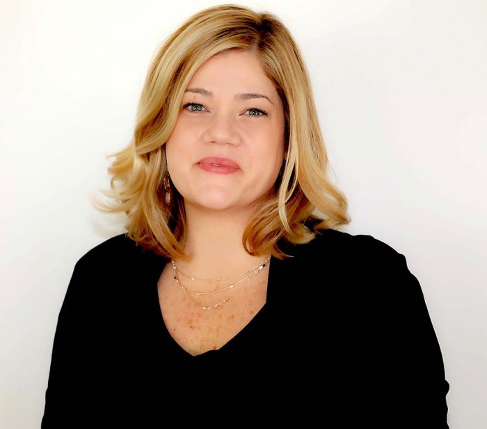 Headshot of blonde Nicole Angarella, wearing black shirt, photographed against white background