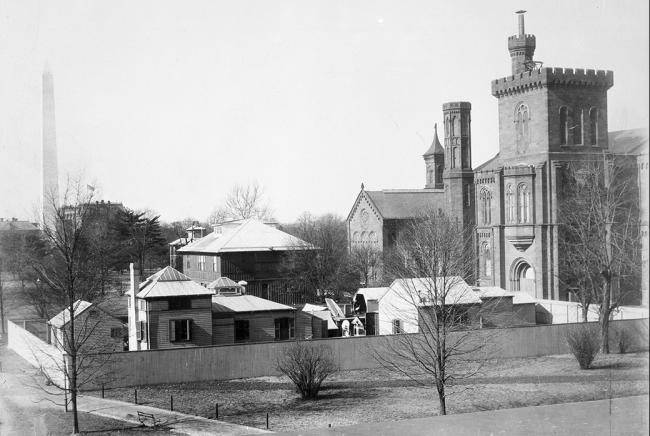 Black and white photo of a collection of small buildings behind the Smithsonian Castle