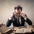 Frazzled man wearing glasses pores overpiles of books