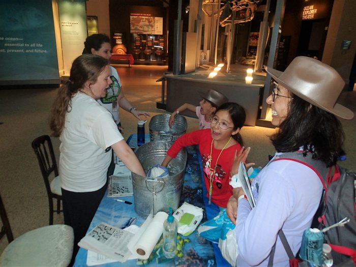 Kids and volunteers laugh as they dip their hands into buckets full of ice