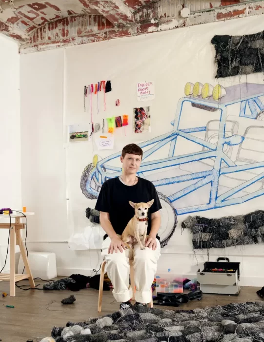 Artist Roberts poses in their studio with a small dog on their lap