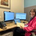 DeCorleto smiles at camera while seated at desk with multiple computer monitors