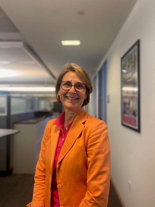 Vertical portrait of Jones in hallway, She is wearing a pink shirt and orange jacket