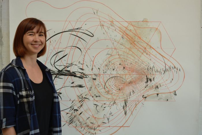 Artist Yulia Pinkusevich standing next to one of her abstract works installed in a gallery