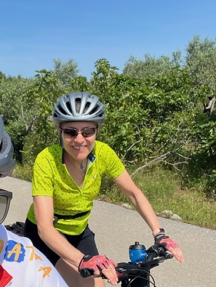 Kathy Sklar, in biking helmet and yellow shirt, pauses for a photo while riding on bike path